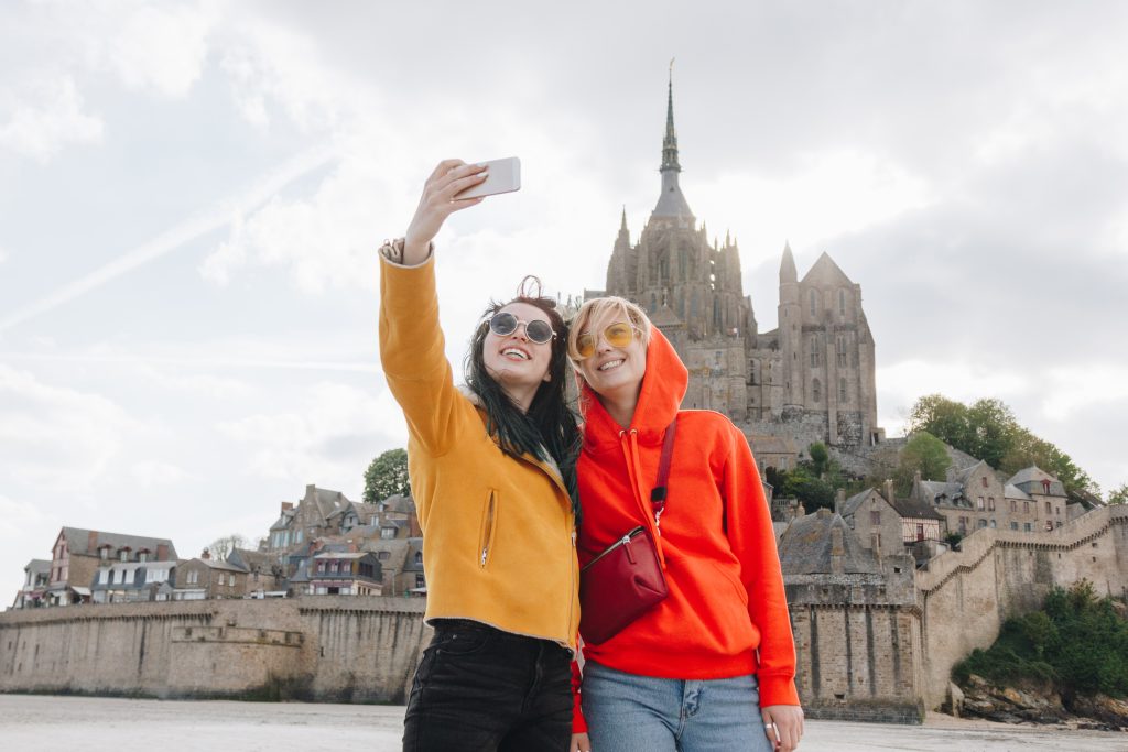 beautiful girls taking selfie on smartphone near saint michaels mount, normandy, france